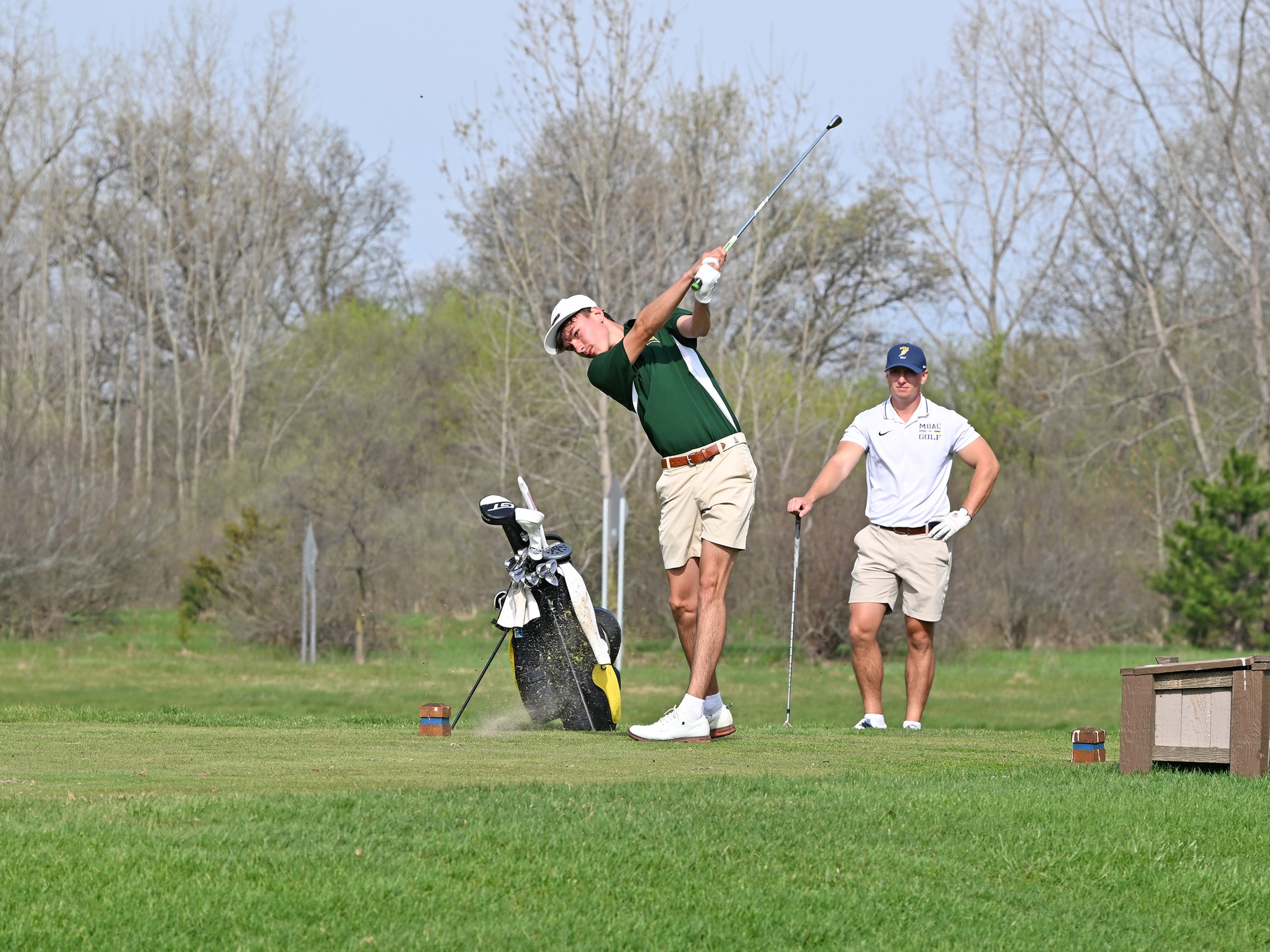 MCC men's golfer swinging a club on the gold course with another teammate standing in the background.
