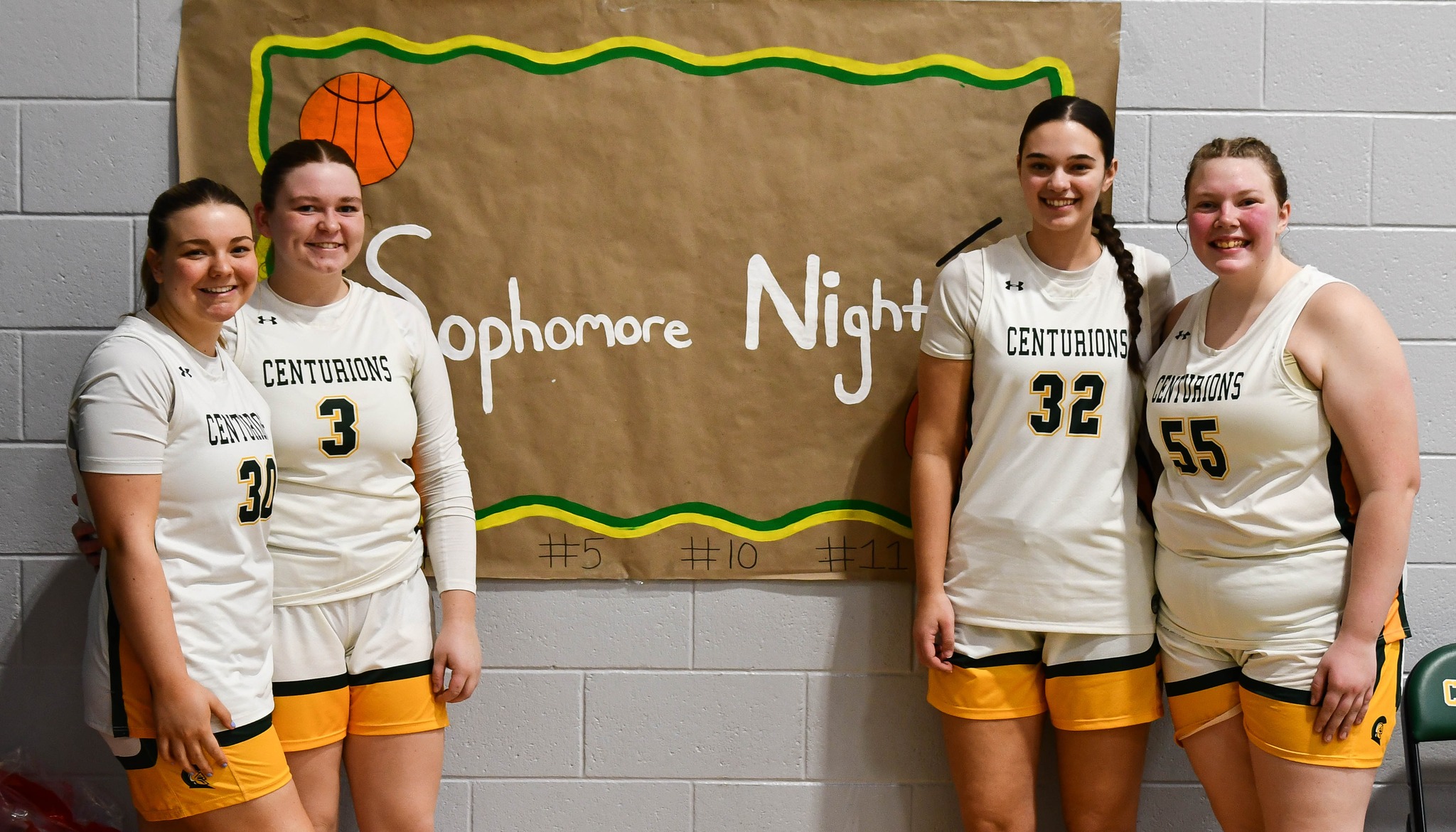 Four MCC women's basketball players standing in front of a sign that reads 